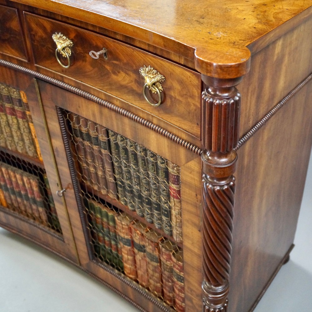 A William IV mahogany side cabinet featuring a concave front, two drawers with circular brass drop handles, and two lower mesh wire grille doors flanked by spiral-turned columns. View V