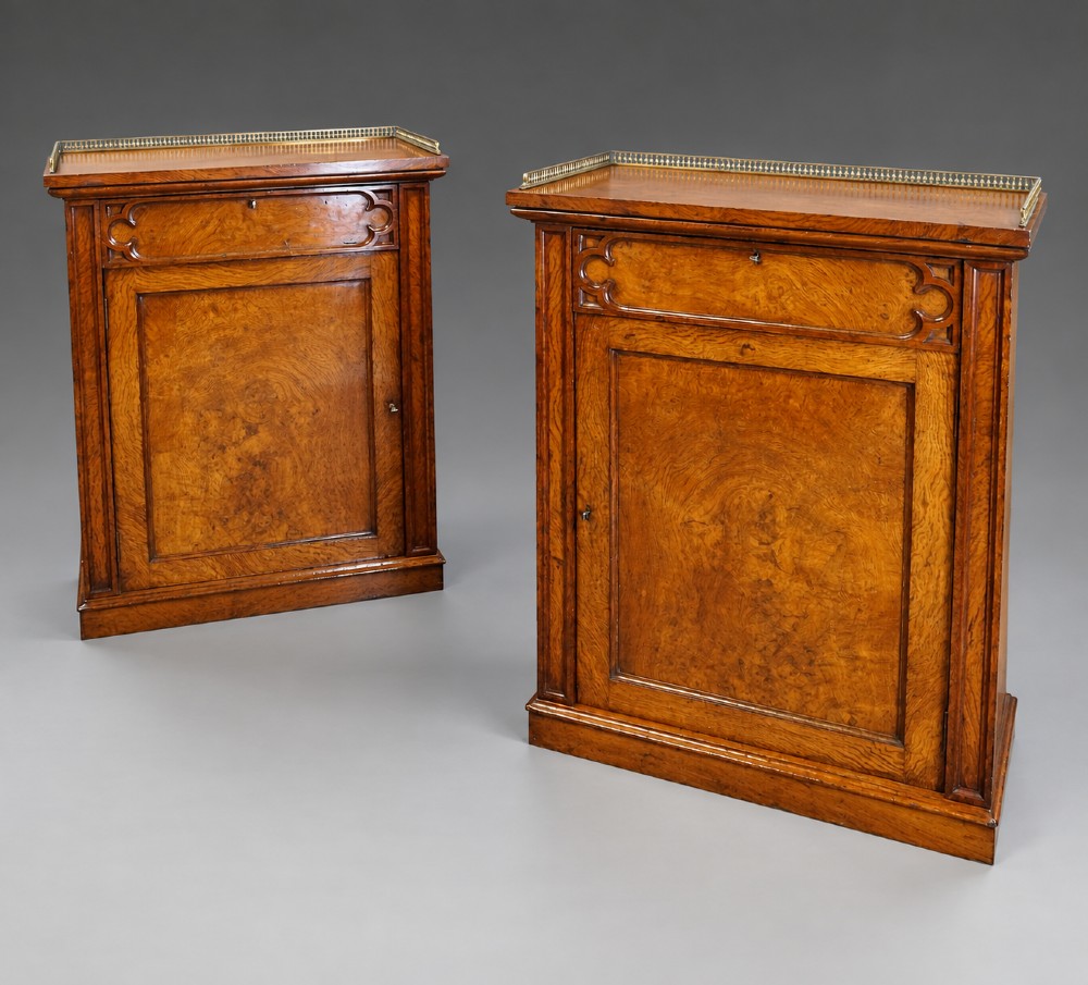 A pair of warm brown Gothic Revival wooden side cabinets featuring carved top drawers, single panel doors, and brass gallery rails along the tops.