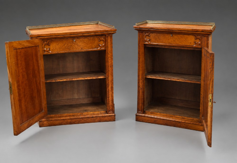 A pair of warm brown Gothic Revival wooden side cabinets featuring carved top drawers, single panel doors, and brass gallery rails along the tops. View VI