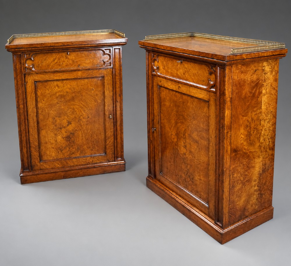 A pair of warm brown Gothic Revival wooden side cabinets featuring carved top drawers, single panel doors, and brass gallery rails along the tops. View VII