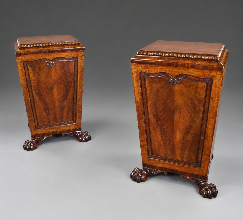 A pair of antique Regency flame mahogany pedestals featuring carved beadwork, framed door panels, and prominent carved lion paw feet.
