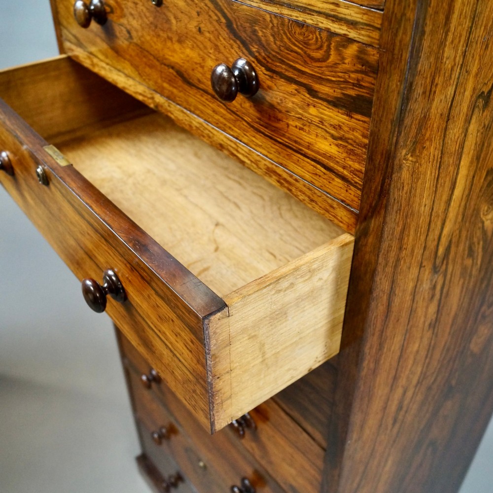 A tall, narrow antique rosewood chest of nine graduated drawers featuring turned wooden knobs and highly figured timber grain. View IV