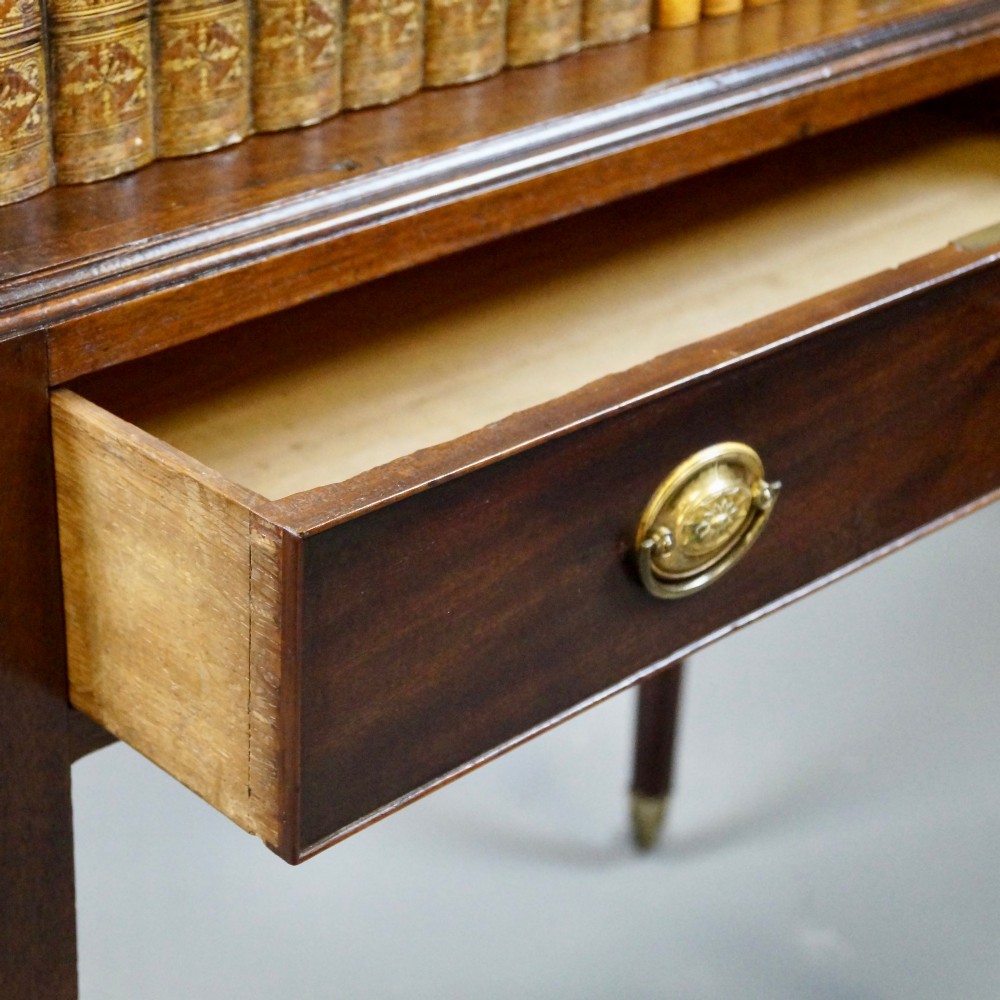 A George III mahogany waterfall bookcase with graduated open shelves, a single base drawer, side brass handles, and tapered square legs on castors. View IV