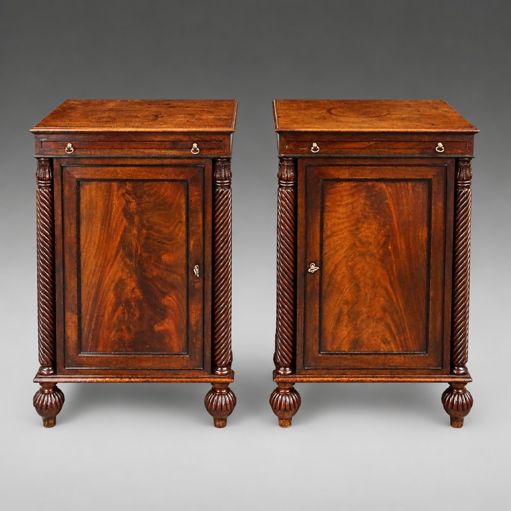 A pair of antique mahogany bedside cupboards with flame mahogany panel doors flanked by spiral-twist columns and supported by lobed bun feet. View II