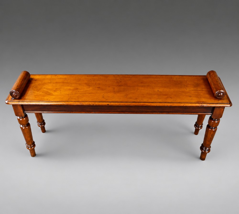 A nineteenth-century mahogany window bench featuring a long rectangular seat with raised scroll ends, supported by four turned legs. View III