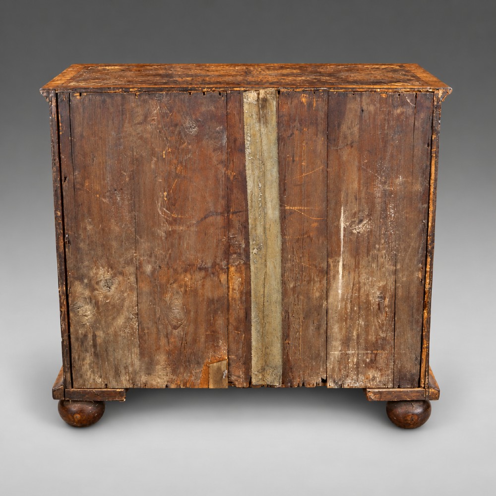 A Queen Anne burr walnut chest of drawers featuring two short over three long graduated drawers with brass drop handles and bun feet. View VI