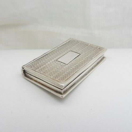 fig 1. An antique sterling silver vinaigrette crafted in the form of a miniature book with an engine-turned cover, rectangular cartouche, and ribbed spine.
