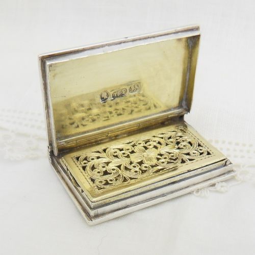An antique sterling silver vinaigrette crafted in the form of a miniature book with an engine-turned cover, rectangular cartouche, and ribbed spine. View VI