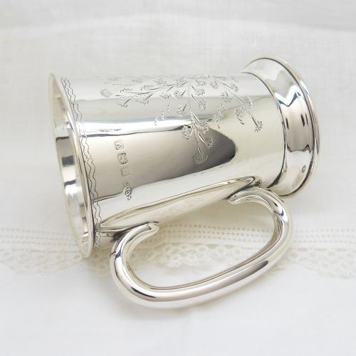 fig 1. An antique sterling silver christening mug featuring an engraved foliage design and a curved handle.