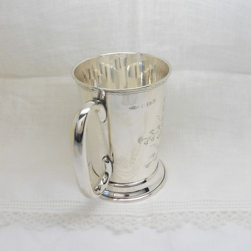An antique sterling silver christening mug featuring an engraved foliage design and a curved handle. View III