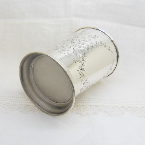 An antique sterling silver christening mug featuring an engraved foliage design and a curved handle. View V