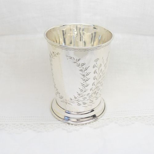 An antique sterling silver christening mug featuring an engraved foliage design and a curved handle. View VI