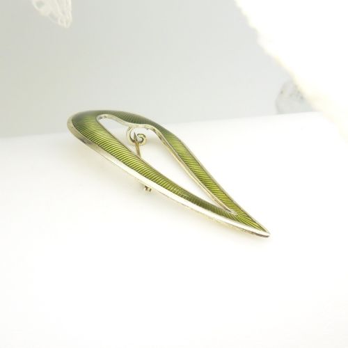 fig 1. An asymmetric leaf-shaped brooch decorated with green guilloche enamel set within a gilded sterling silver frame.