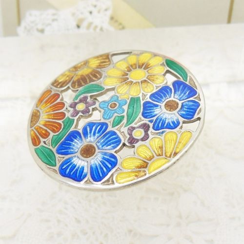 A circular sterling silver brooch featuring colourful enamelled flowers in shades of blue, yellow, orange, and purple with green leaves. View II