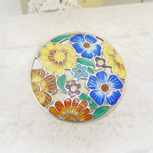 A circular sterling silver brooch featuring colourful enamelled flowers in shades of blue, yellow, orange, and purple with green leaves. View IV
