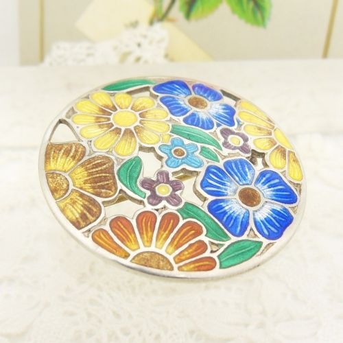 A circular sterling silver brooch featuring colourful enamelled flowers in shades of blue, yellow, orange, and purple with green leaves. View V