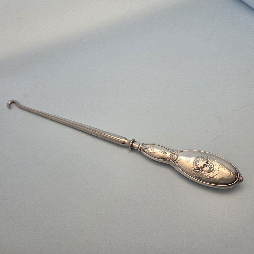 An Edwardian sterling silver button hook handle decorated with an embossed cherub face surrounded by wings and floral scrolls. View IV