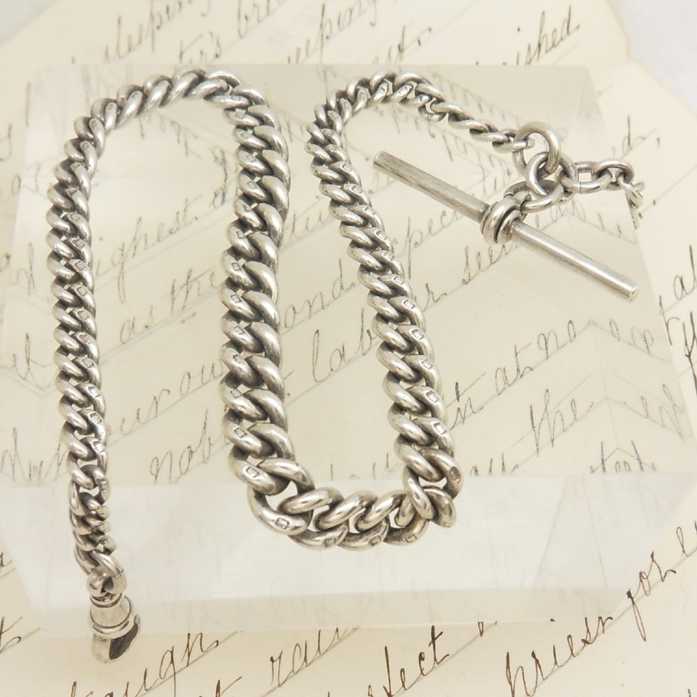 A sterling silver heavy curb link pocket watch chain featuring a T-bar attachment and swivel clasp laid across a surface.