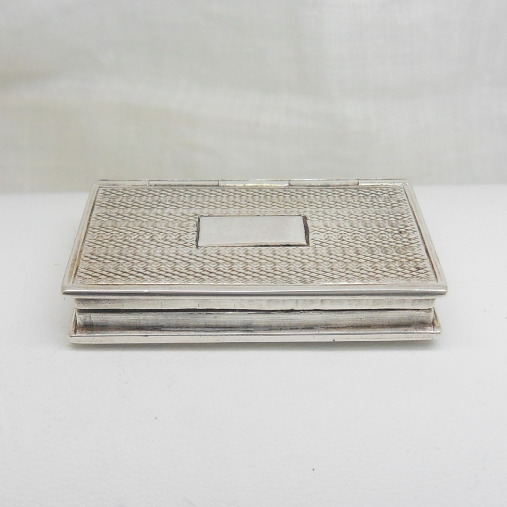 An antique sterling silver vinaigrette crafted in the form of a miniature book with an engine-turned cover, rectangular cartouche, and ribbed spine. View III