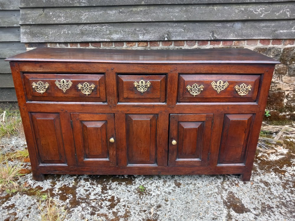 An eighteenth-century dark oak dresser base featuring three drawers with pierced brass handles situated above panelled cupboard doors.