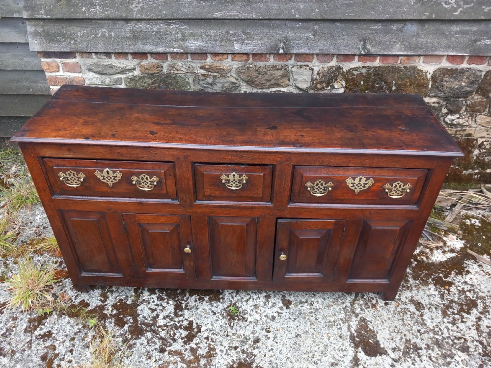 An eighteenth-century dark oak dresser base featuring three drawers with pierced brass handles situated above panelled cupboard doors. View III