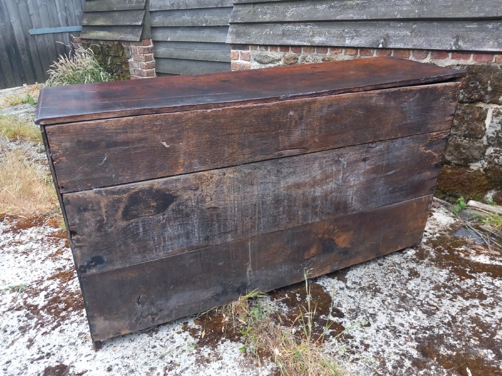 An eighteenth-century dark oak dresser base featuring three drawers with pierced brass handles situated above panelled cupboard doors. View IV