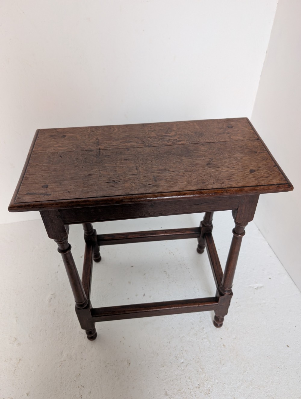 An 18th-century dark oak joint stool featuring turned legs, pegged mortise and tenon joints, and a rectangular top with low stretchers. View VII