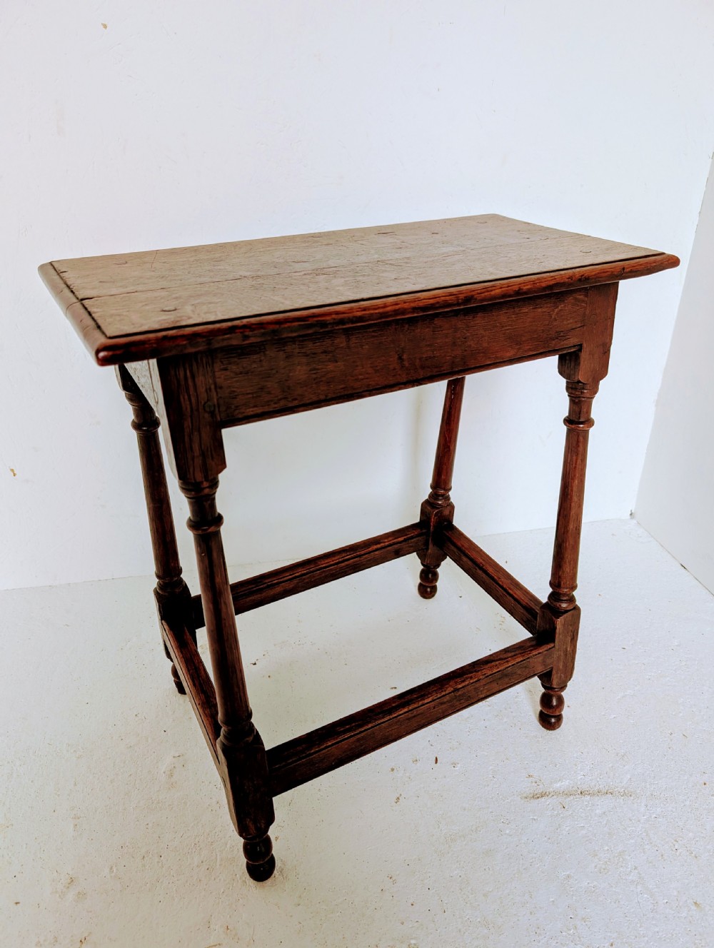 An 18th-century dark oak joint stool featuring turned legs, pegged mortise and tenon joints, and a rectangular top with low stretchers. View IX