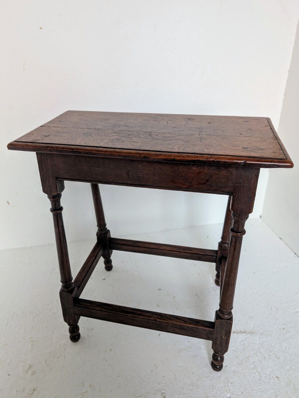 An 18th-century dark oak joint stool featuring turned legs, pegged mortise and tenon joints, and a rectangular top with low stretchers. View X
