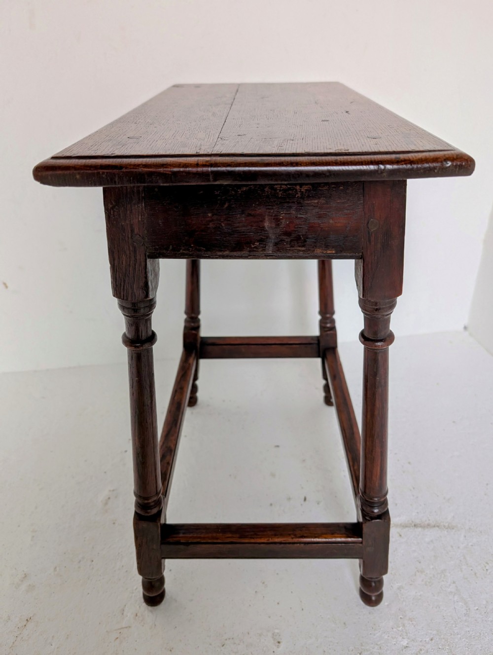 An 18th-century dark oak joint stool featuring turned legs, pegged mortise and tenon joints, and a rectangular top with low stretchers. View XI