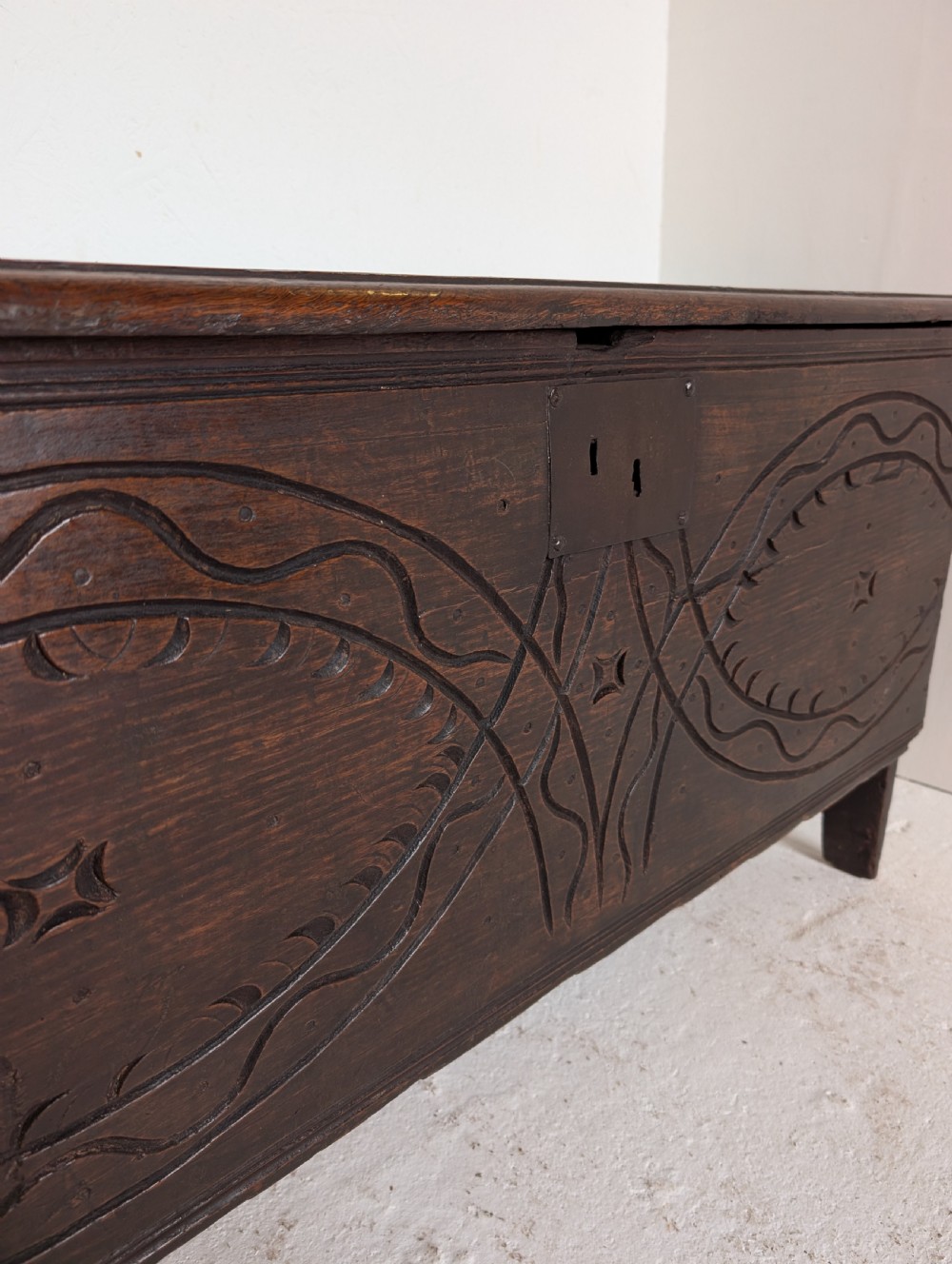 A dark oak 17th-century coffer featuring geometric hand-carved details across the front, an iron lock plate, and stile feet. View VI