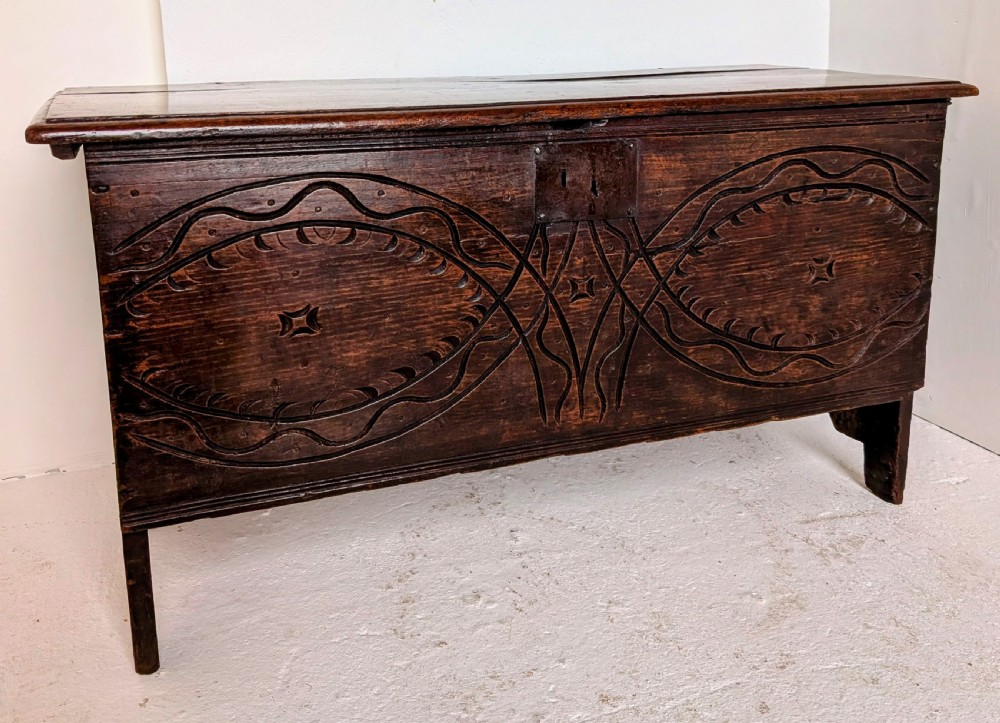 A dark oak 17th-century coffer featuring geometric hand-carved details across the front, an iron lock plate, and stile feet.