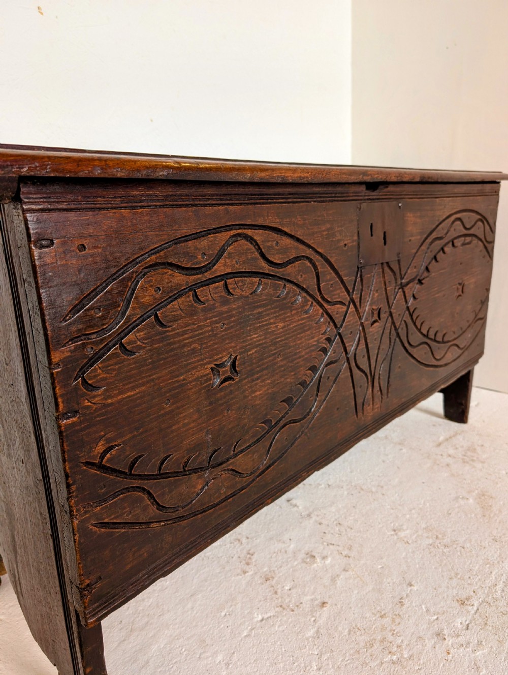 A dark oak 17th-century coffer featuring geometric hand-carved details across the front, an iron lock plate, and stile feet. View X