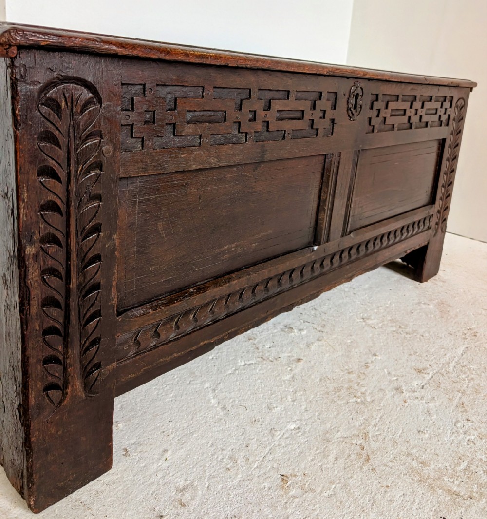 A seventeenth-century dark oak coffer featuring carved leaf stiles, geometric fretwork, and a panelled front structure. View II