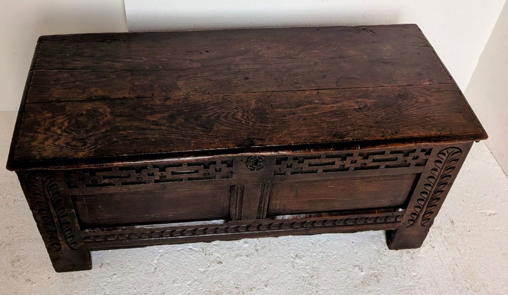 A seventeenth-century dark oak coffer featuring carved leaf stiles, geometric fretwork, and a panelled front structure. View III