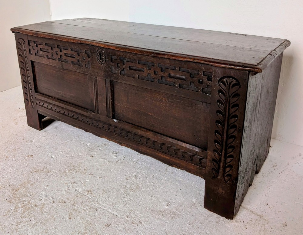 A seventeenth-century dark oak coffer featuring carved leaf stiles, geometric fretwork, and a panelled front structure. View V