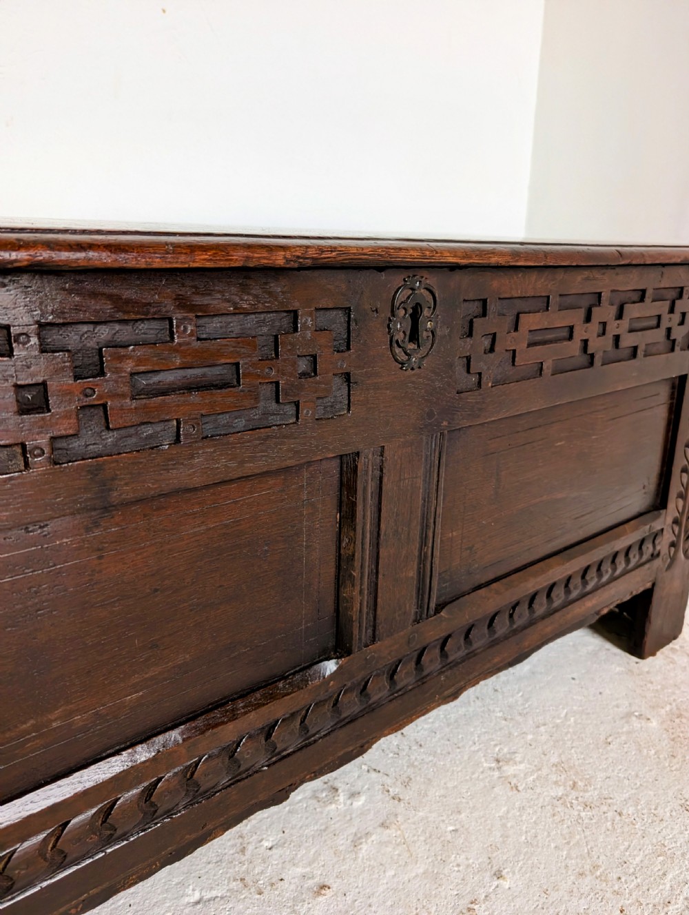 A seventeenth-century dark oak coffer featuring carved leaf stiles, geometric fretwork, and a panelled front structure. View VI