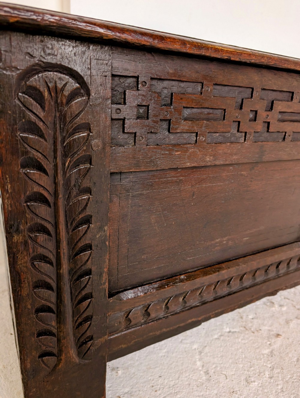 A seventeenth-century dark oak coffer featuring carved leaf stiles, geometric fretwork, and a panelled front structure. View VII