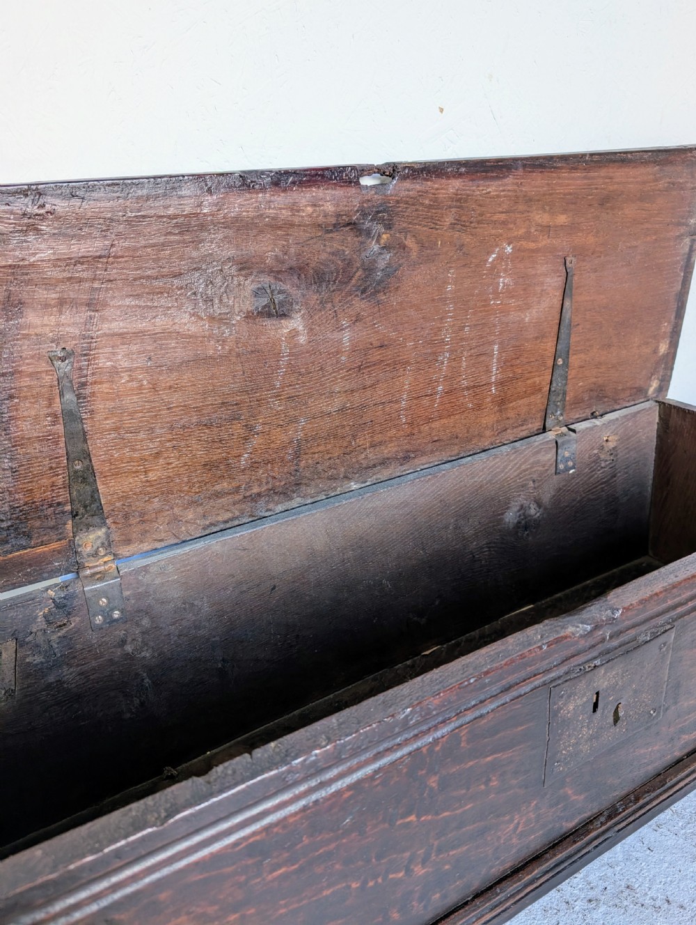 A small 17th-century dark oak plank coffer featuring a hinged rectangular lid, iron escutcheon plate, and V-shaped end supports. View II