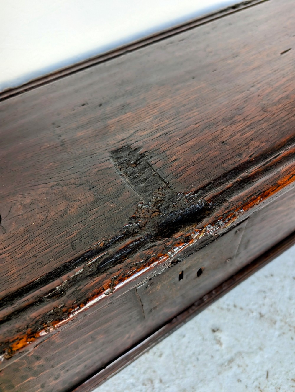 A small 17th-century dark oak plank coffer featuring a hinged rectangular lid, iron escutcheon plate, and V-shaped end supports. View IV