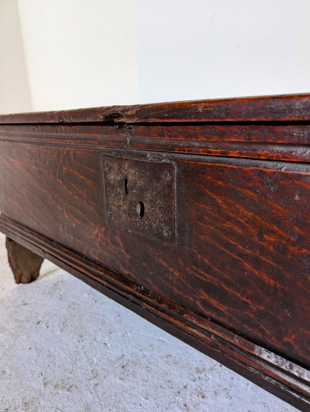 A small 17th-century dark oak plank coffer featuring a hinged rectangular lid, iron escutcheon plate, and V-shaped end supports. View VIII