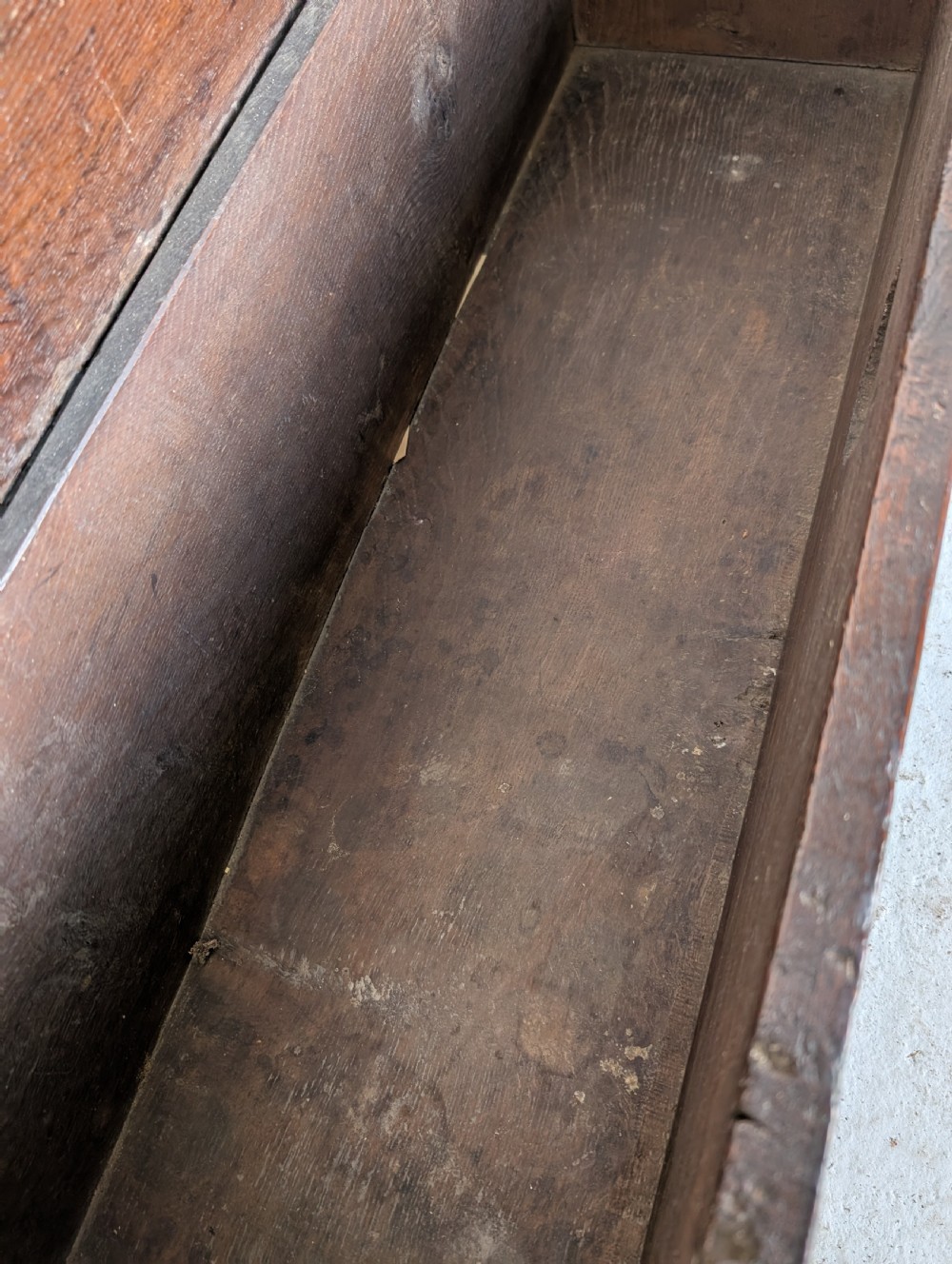 A small 17th-century dark oak plank coffer featuring a hinged rectangular lid, iron escutcheon plate, and V-shaped end supports. View IX