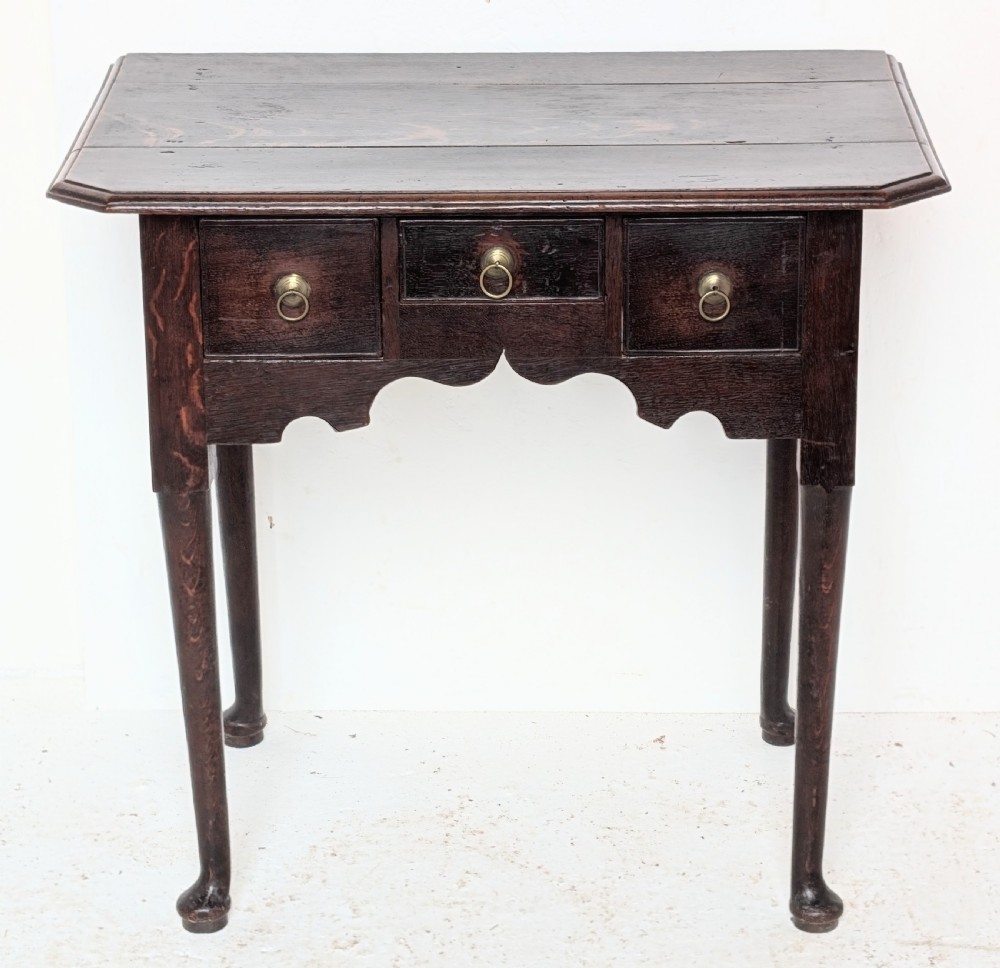 An 18th-century dark oak lowboy table featuring three drawers with brass ring pulls, a scalloped apron, and cabriole legs ending in pad feet.