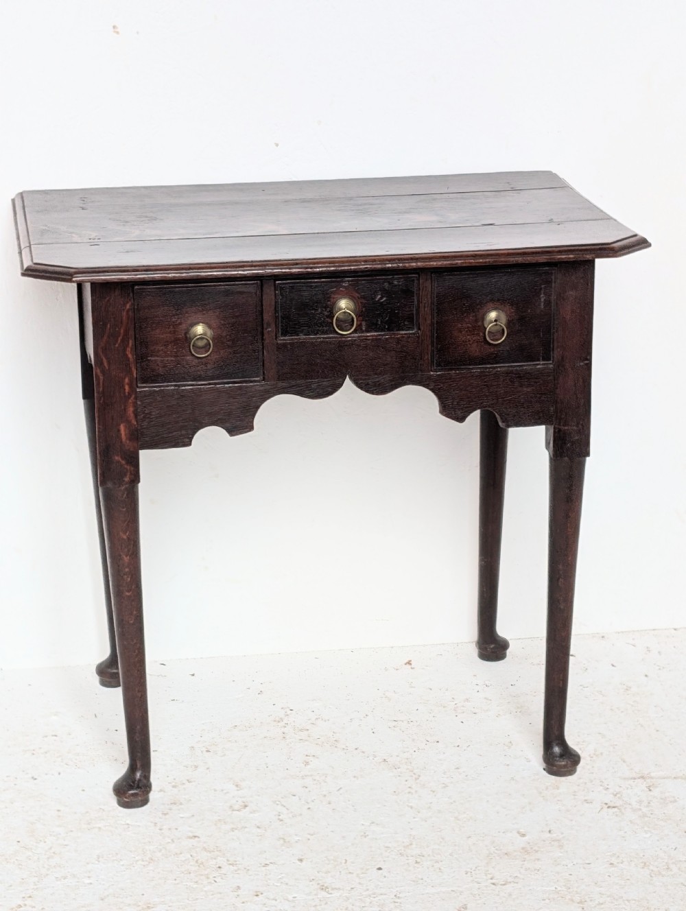 An 18th-century dark oak lowboy table featuring three drawers with brass ring pulls, a scalloped apron, and cabriole legs ending in pad feet. View II