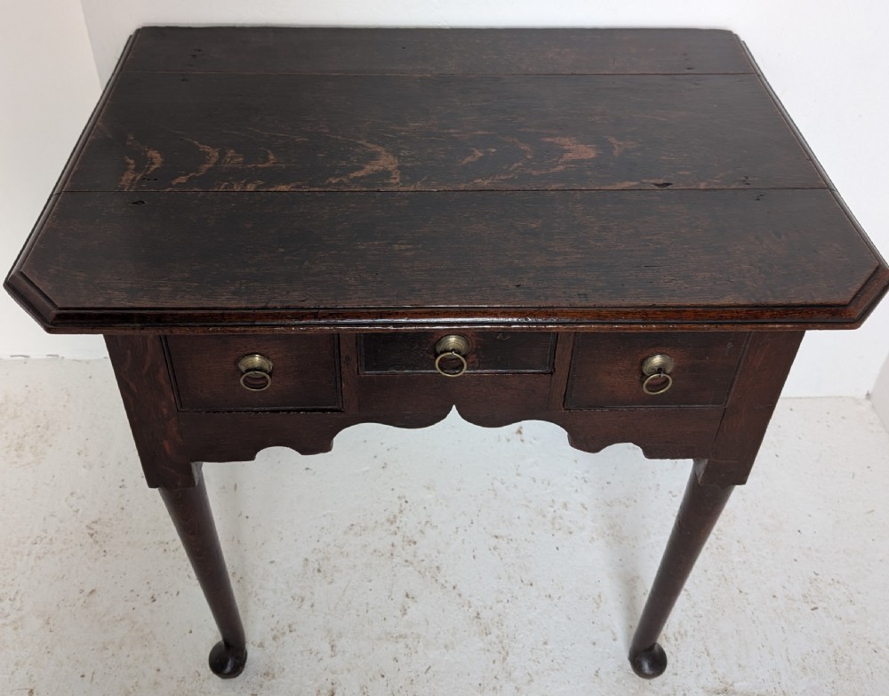 An 18th-century dark oak lowboy table featuring three drawers with brass ring pulls, a scalloped apron, and cabriole legs ending in pad feet. View III