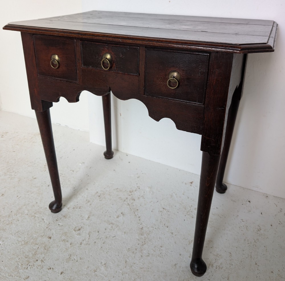 An 18th-century dark oak lowboy table featuring three drawers with brass ring pulls, a scalloped apron, and cabriole legs ending in pad feet. View IV