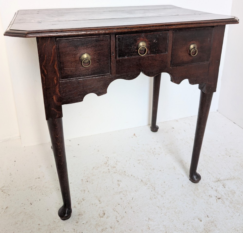 An 18th-century dark oak lowboy table featuring three drawers with brass ring pulls, a scalloped apron, and cabriole legs ending in pad feet. View V