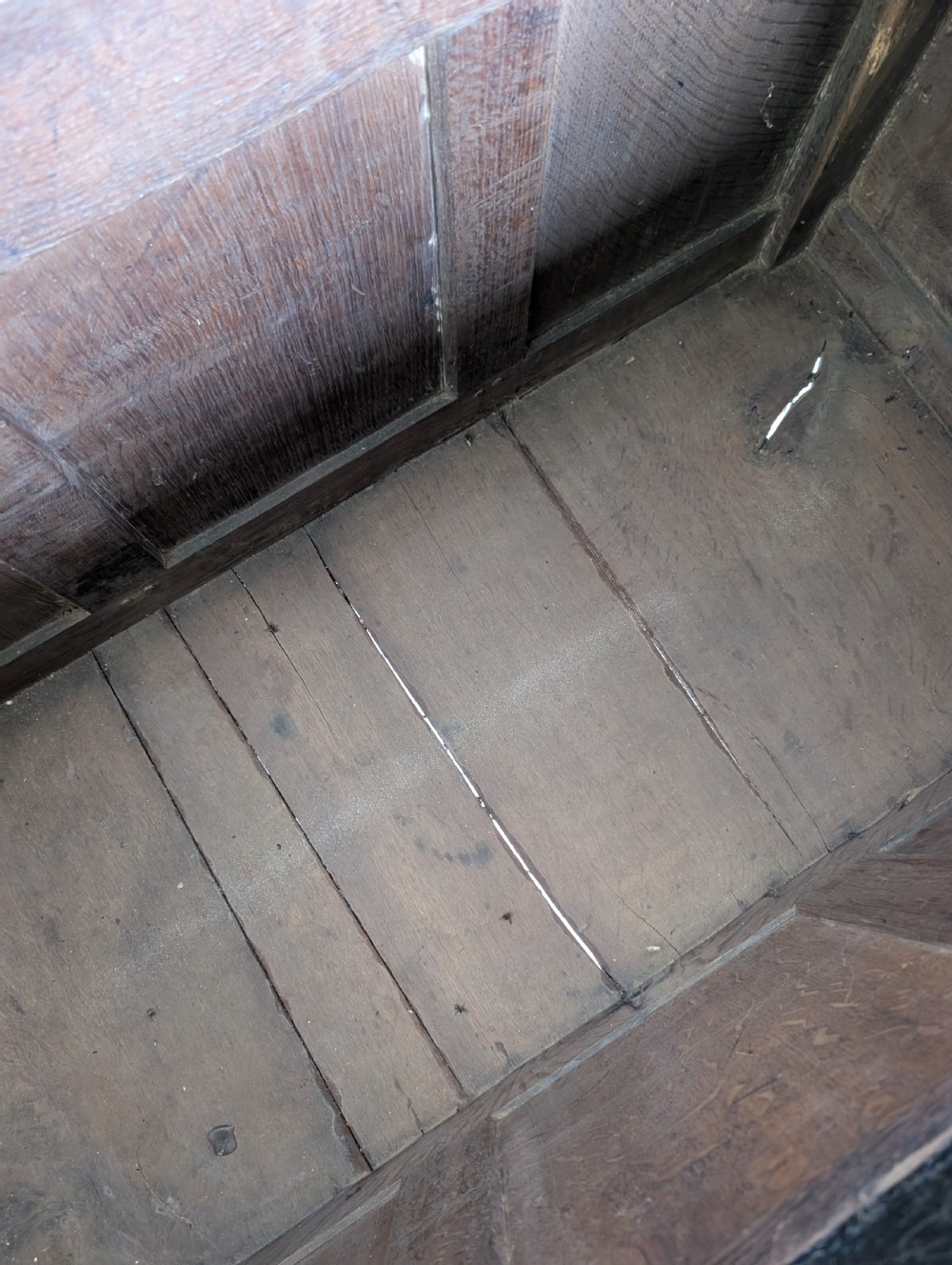 A dark oak 17th-century coffer featuring three front panels and a carved scrollwork frieze below the hinged lid. View III