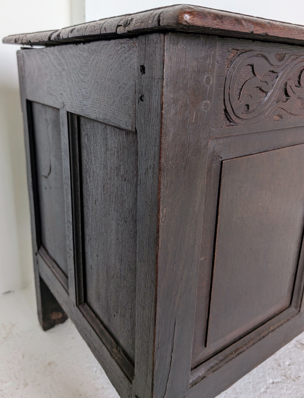 A dark oak 17th-century coffer featuring three front panels and a carved scrollwork frieze below the hinged lid. View IV
