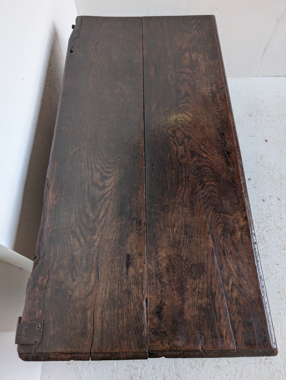 A dark oak 17th-century coffer featuring three front panels and a carved scrollwork frieze below the hinged lid. View VI